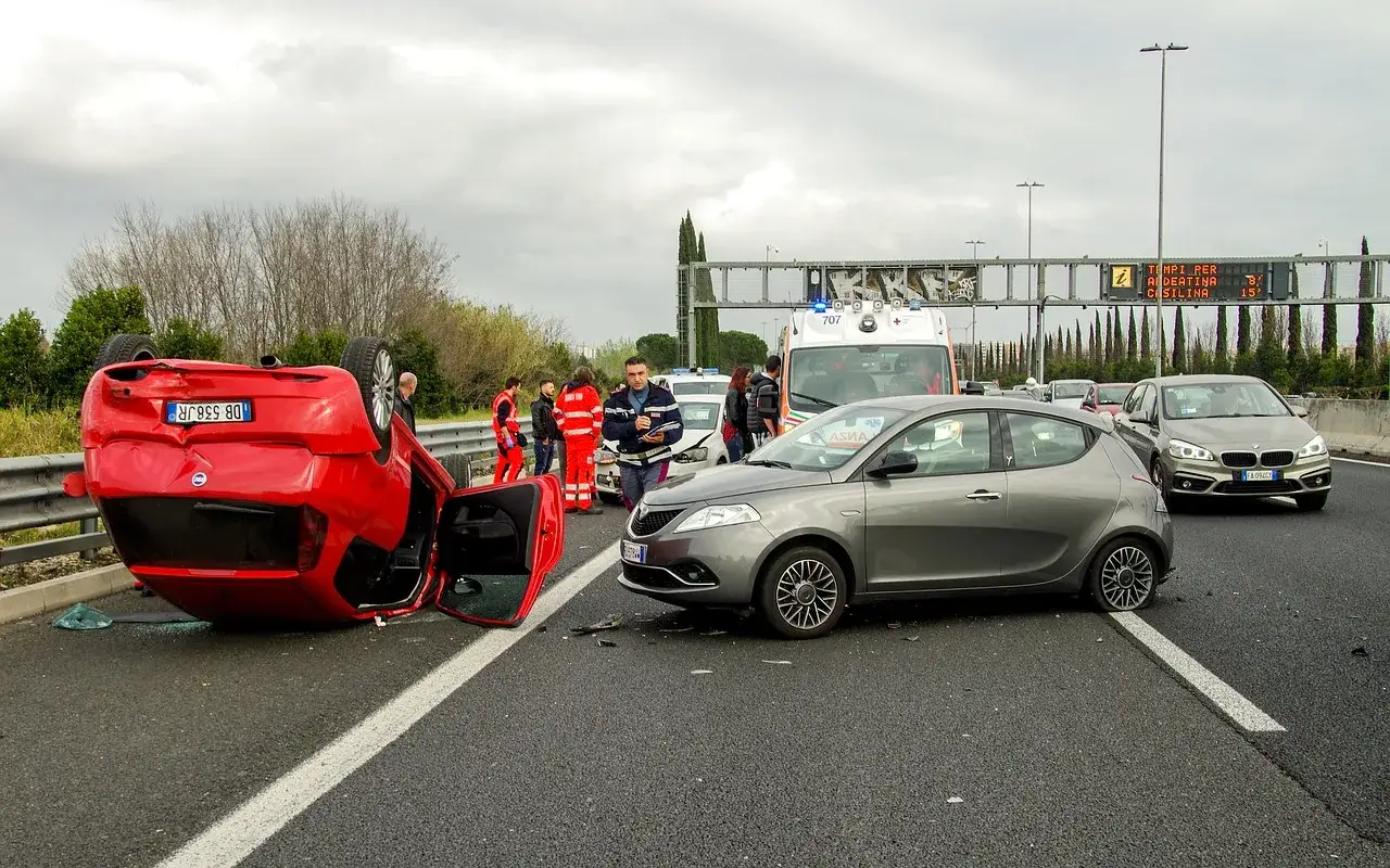 Wypadek na autostradzie. Przewrócony czerwony samochód, karetka i policja. Kierowca może otrzymać mandat za kolizje.