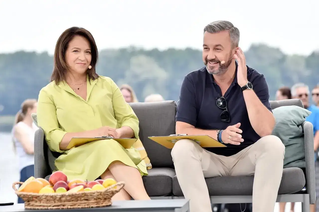 Krzysztof Skórzyński, ile ma lat? Dziennikarz z uśmiechem siedzi obok koleżanki, trzymając notatki.