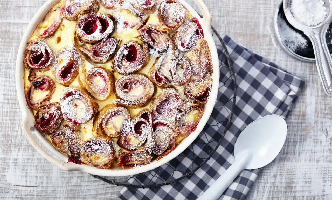 Ein Auflauf mit gerollten Pfannkuchen, gefüllt mit Kirschen und bestäubt mit Puderzucker. Ein köstliches Pfannkuchen Rezept!
