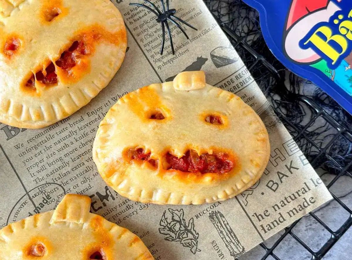 Gruselige Kürbis-Pasteten, perfekt für Halloween-Rezepte. Kleine, gefüllte Teigtaschen mit grinsenden Gesichtern.