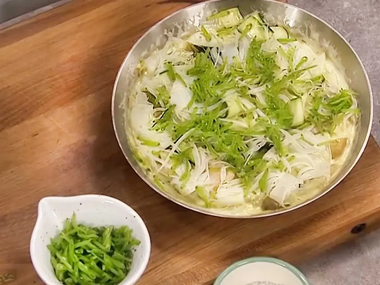 En panna med vit fisk och grönsaker, toppad med strimlad grönkål. En liten skål med gröna strimlor står bredvid.