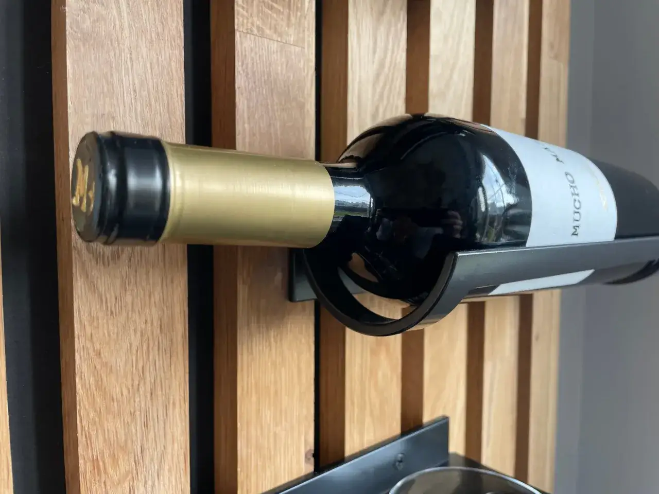 Elegancki stojak na wino z czarnego metalu, na drewnianej ściance, prezentuje butelkę czerwonego wina z etykietą 