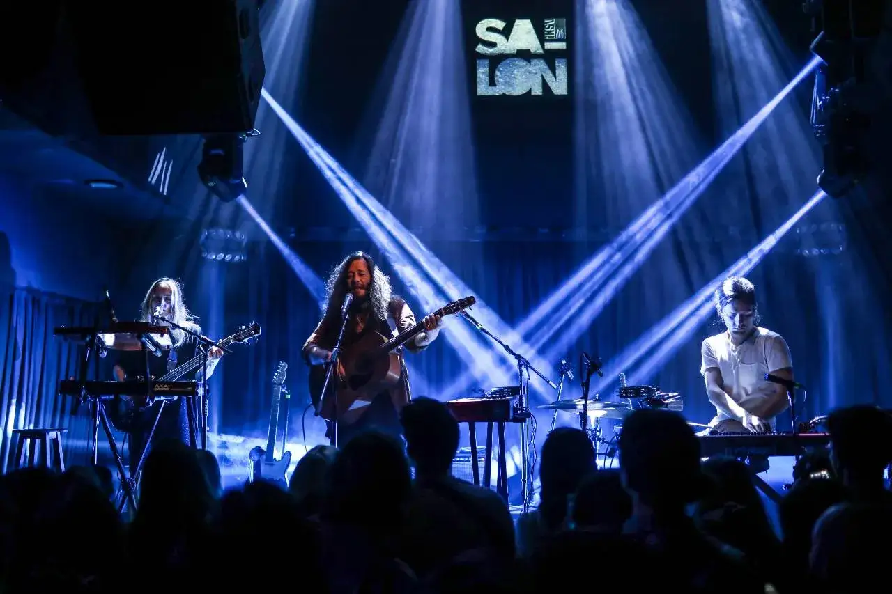 Zespół grający shoegaze na scenie, oświetlony niebieskimi światłami. Wokalista z gitarą akustyczną, klawiszowiec i gitarzystka.