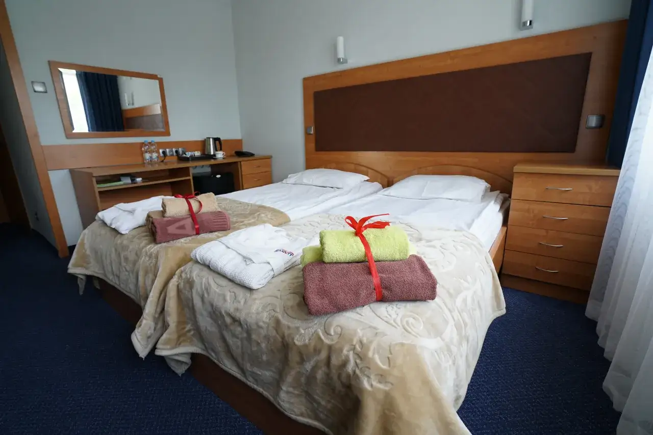 Pokój w sanatorium Sanvit Ciechocinek z dwoma łóżkami, ręcznikami i szlafrokami.