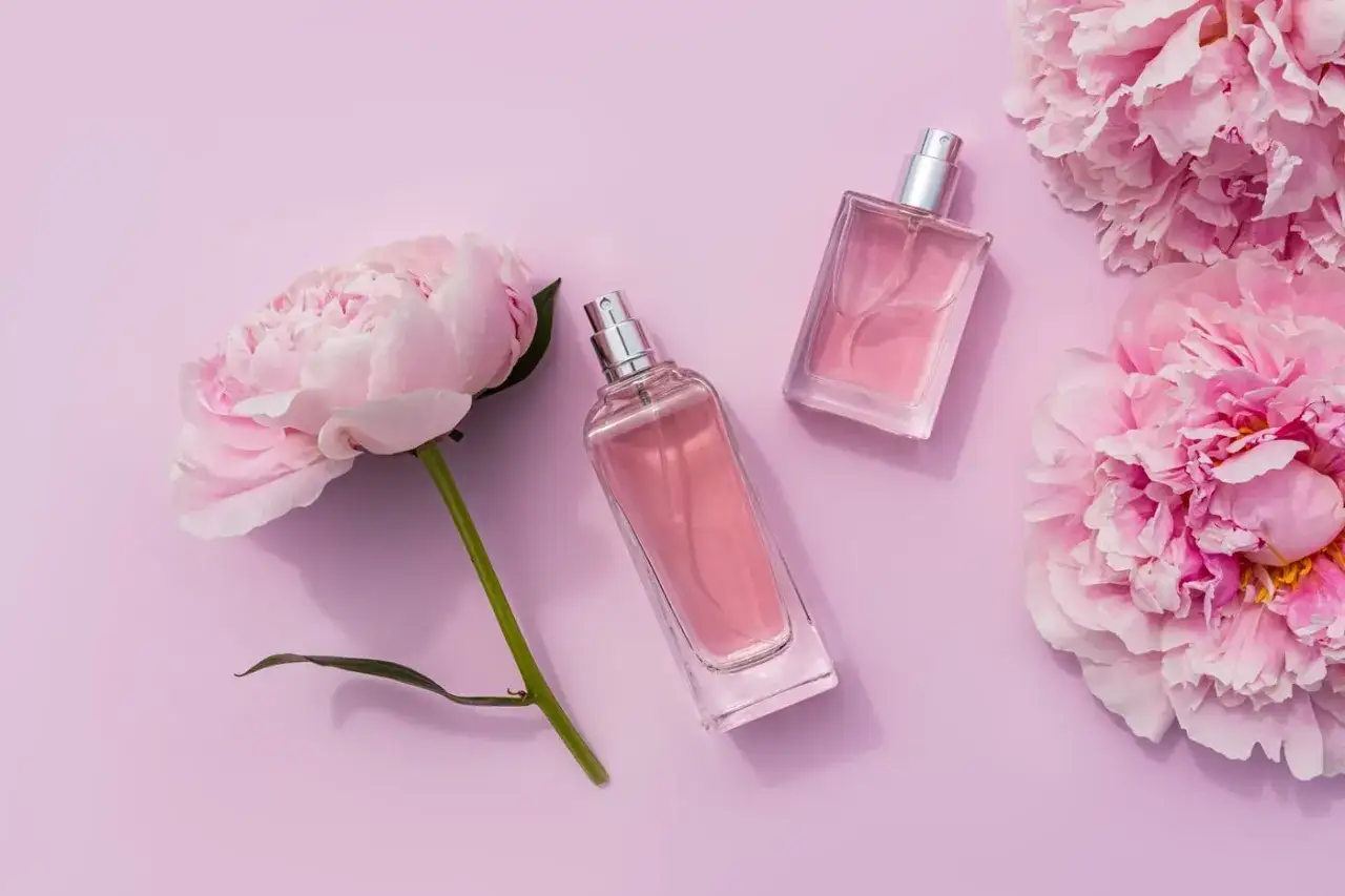 Dwa flakoniki różowych perfum i delikatne pivoine na pastelowym tle.