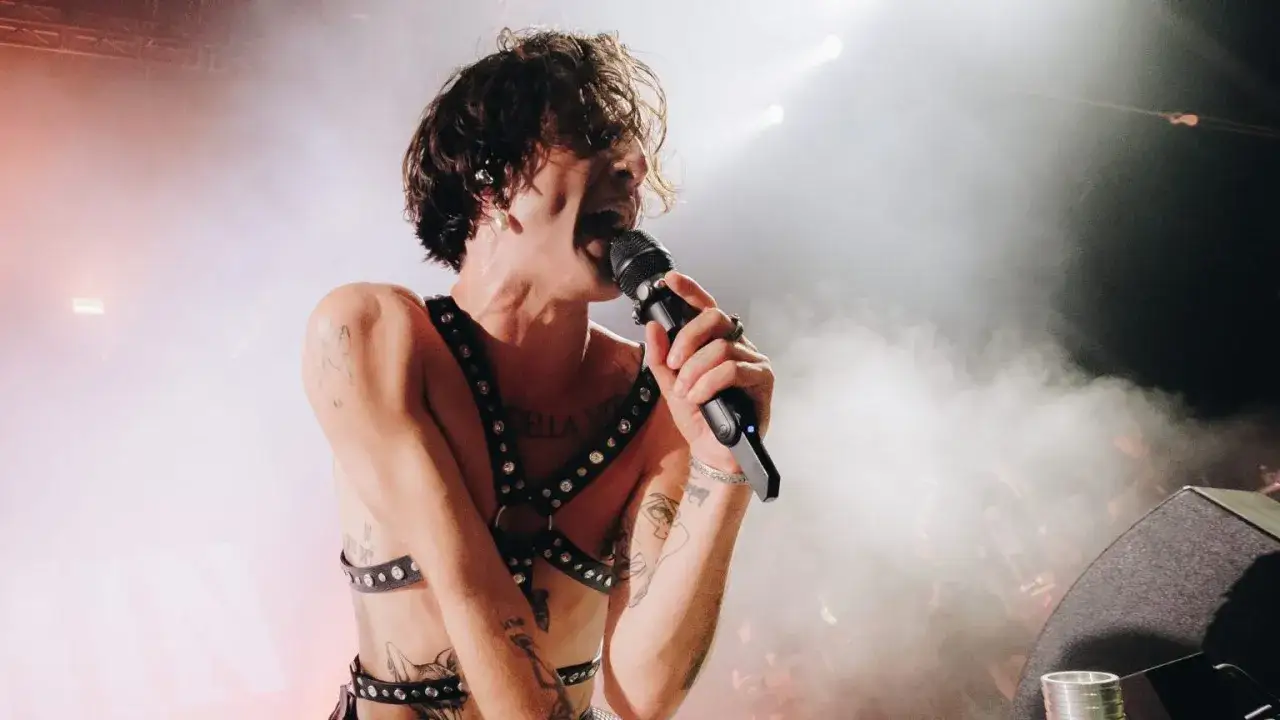 Le chanteur rock italien, torse nu et portant un harnais clout&eacute;, chante passionn&eacute;ment dans un microphone sur sc&egrave;ne, entour&eacute; de fum&eacute;e et de lumi&egrave;res.