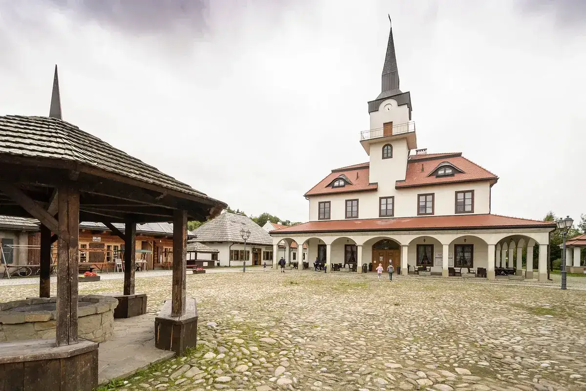 Urokliwe miasteczko galicyjskie skansen z brukowanym rynkiem, studnią i budynkami z wieżą.