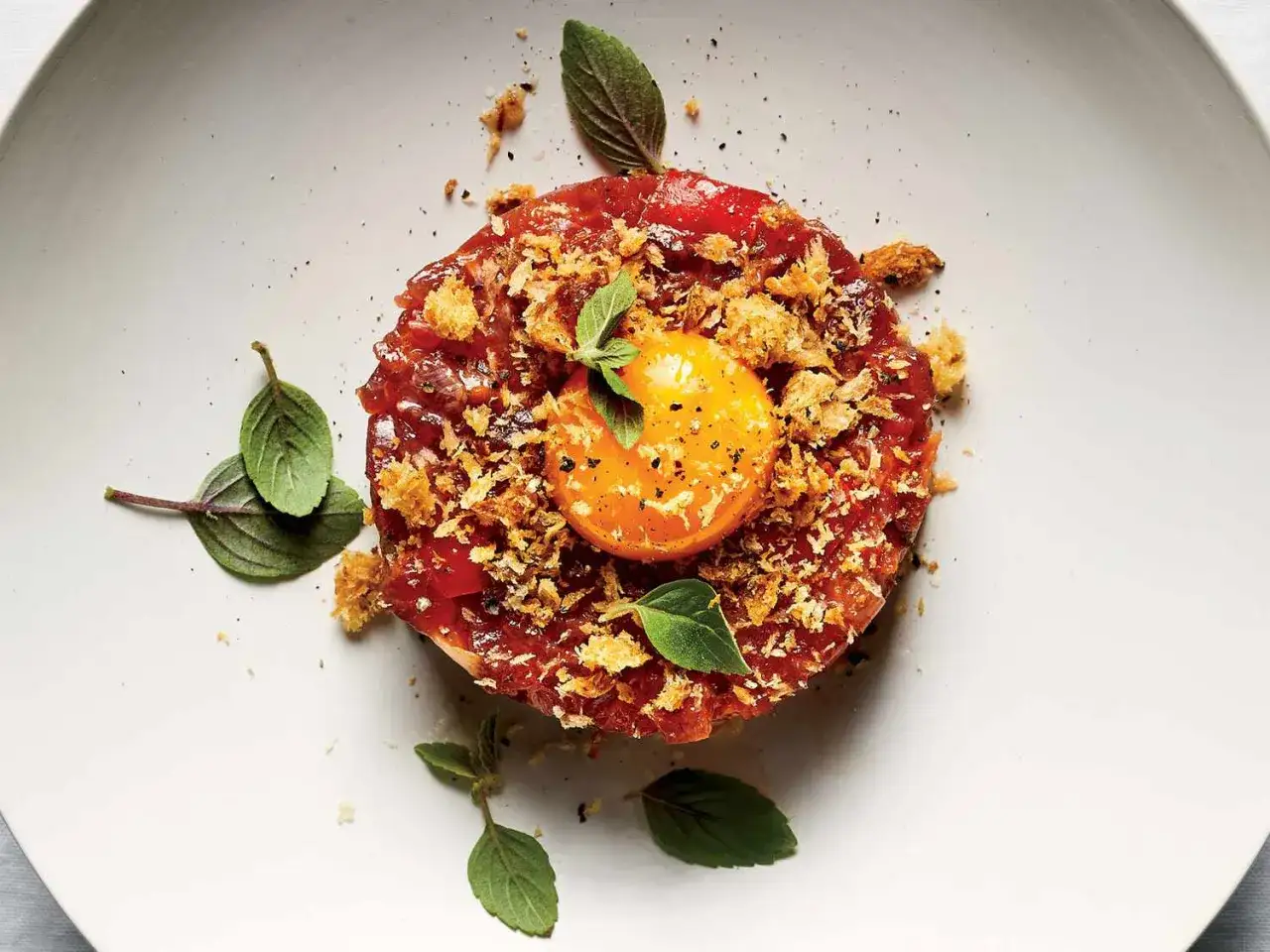Delicioso steak tartar, una receta original con yema de huevo, crujientes y hojas verdes.