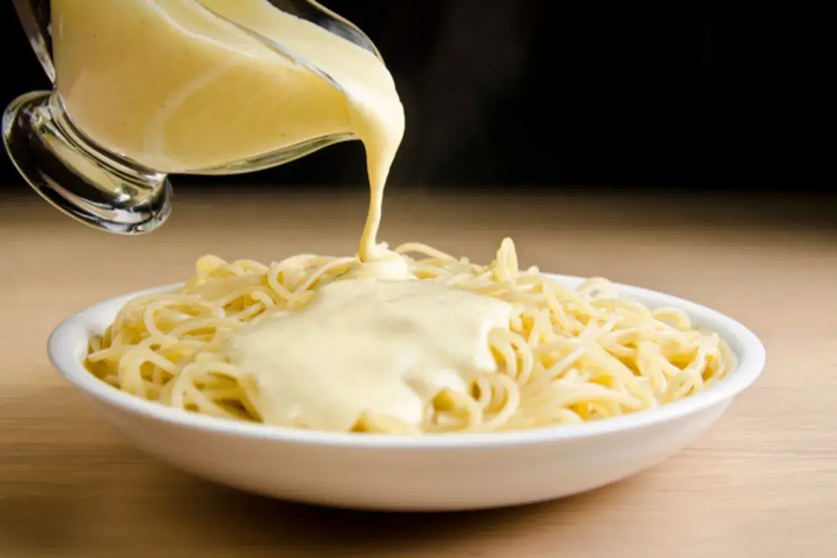 Gęsty, kremowy sos spływa z sosjerki na talerz pełen spaghetti. Idealny sposób, jak zagęścić sos do makaronu.