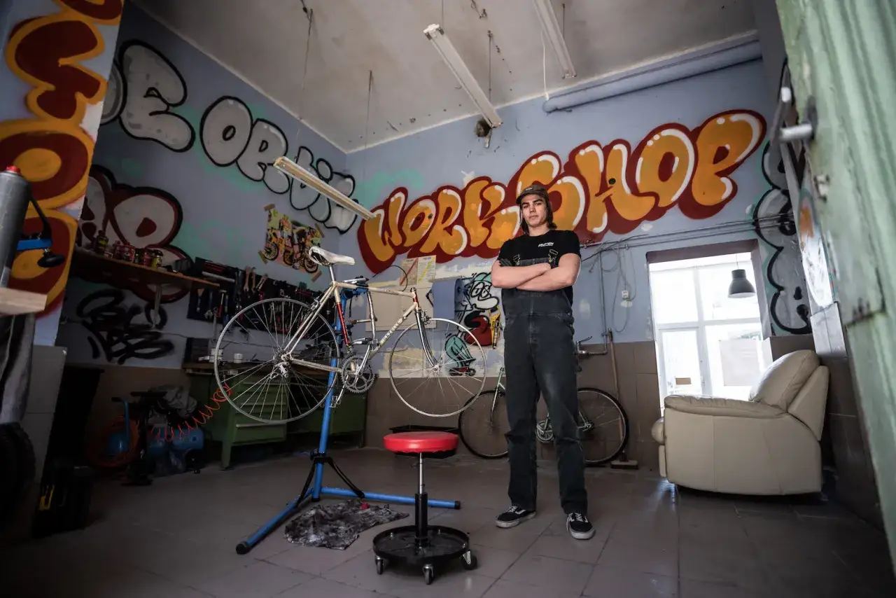 Młody mechanik w warsztacie z graffiti, obok rower na stojaku. Inspiracje i części do renowacji starego roweru do jazdy miejskiej.