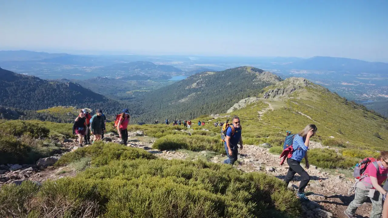 Un grupo de excursionistas sigue una cuerda larga ruta por una montaña con vistas a un valle y un lago.