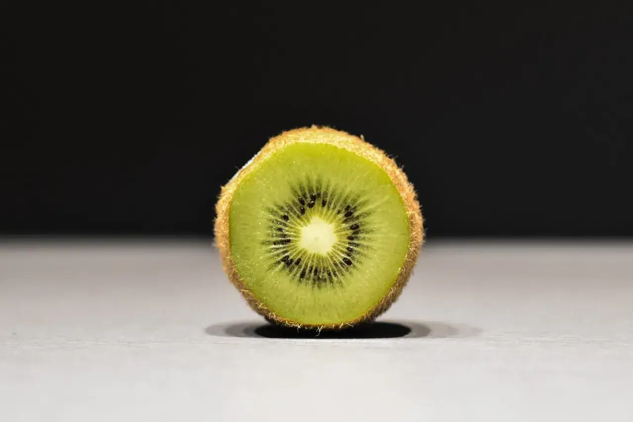 Przekrojone kiwi, idealne na keto. Soczyste, zielone wnętrze z czarnymi pestkami, otoczone brązową, włochatą skórką.