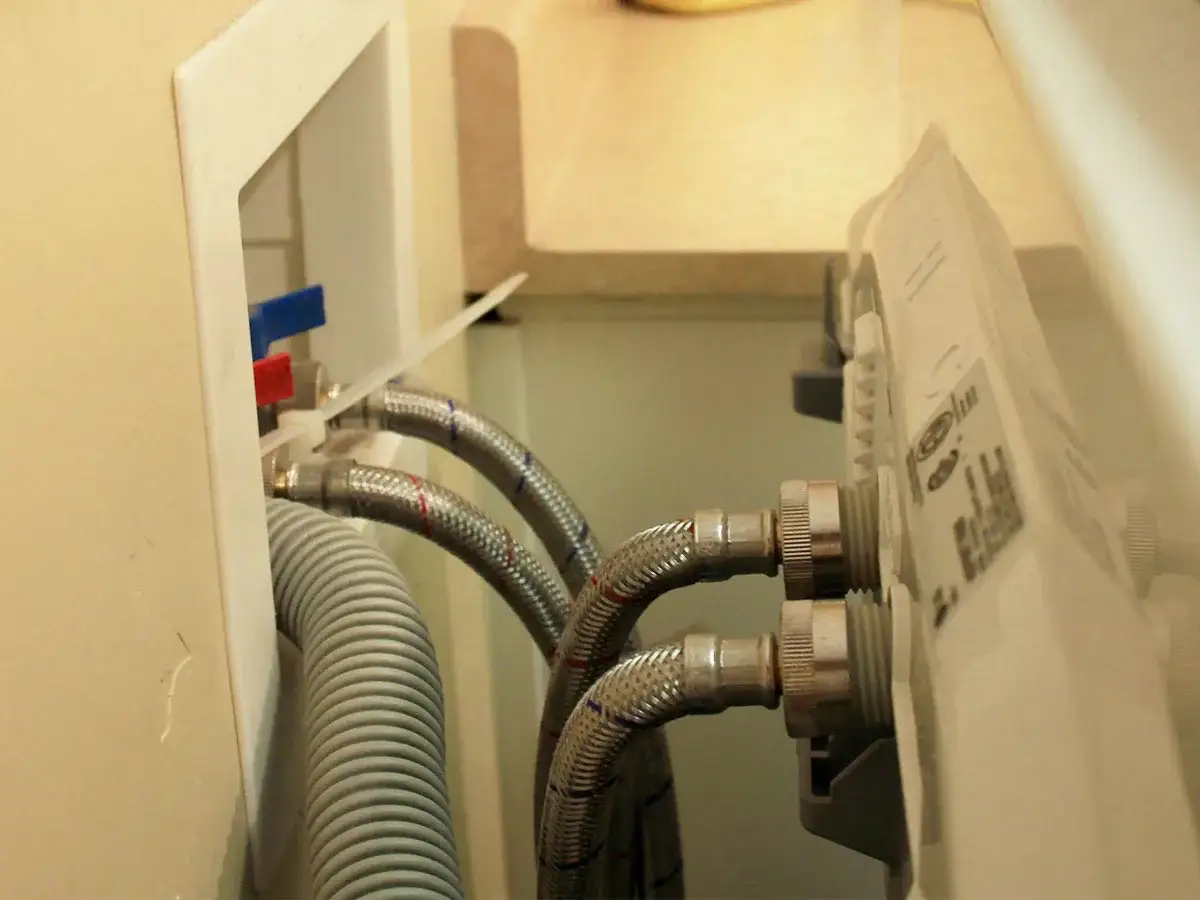Connecting water hoses for washing machine installation. Red and blue valves are visible.