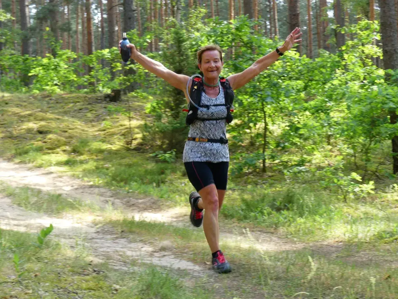 Uśmiechnięta biegaczka z radością pokonuje leśny szlak podczas rykowisko ultra trail.