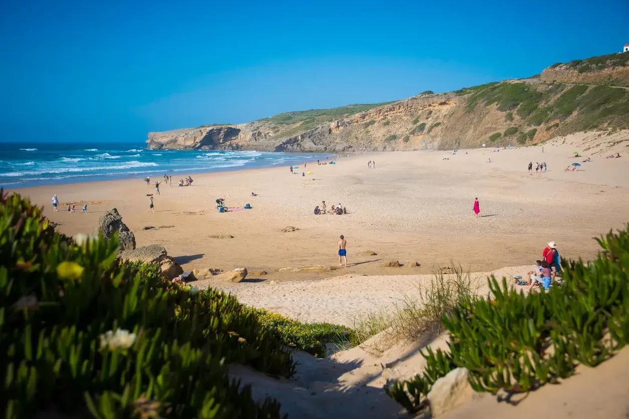 Sonniger Strand bei Monte Clerigo mit Menschen, die sich am Meer und im Sand vergnügen.