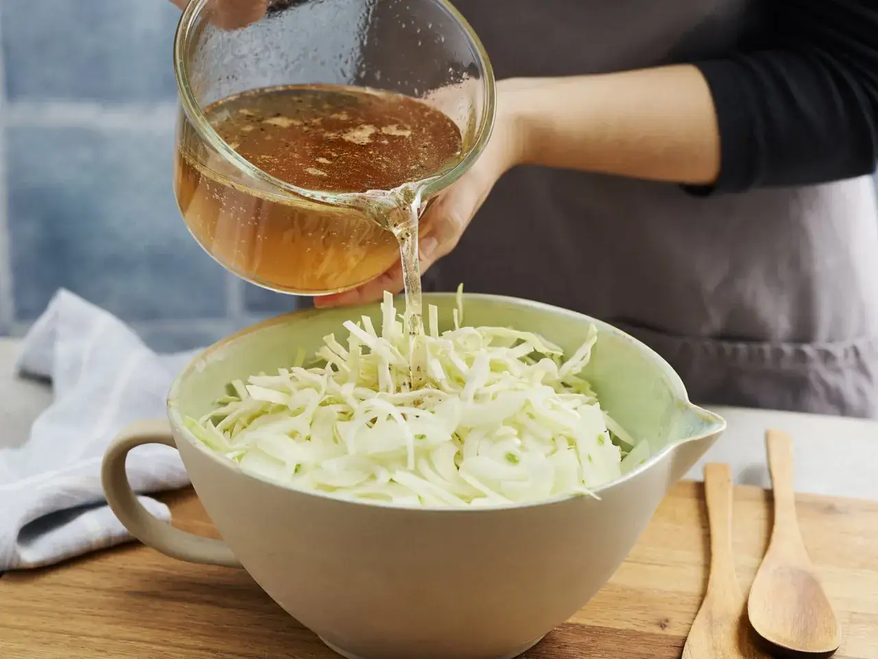 Eine Person gie&szlig;t eine braune Fl&uuml;ssigkeit &uuml;ber fein geschnittenen Kohl und Zwiebeln in einer Sch&uuml;ssel, um einen griechischen Krautsalat zuzubereiten.