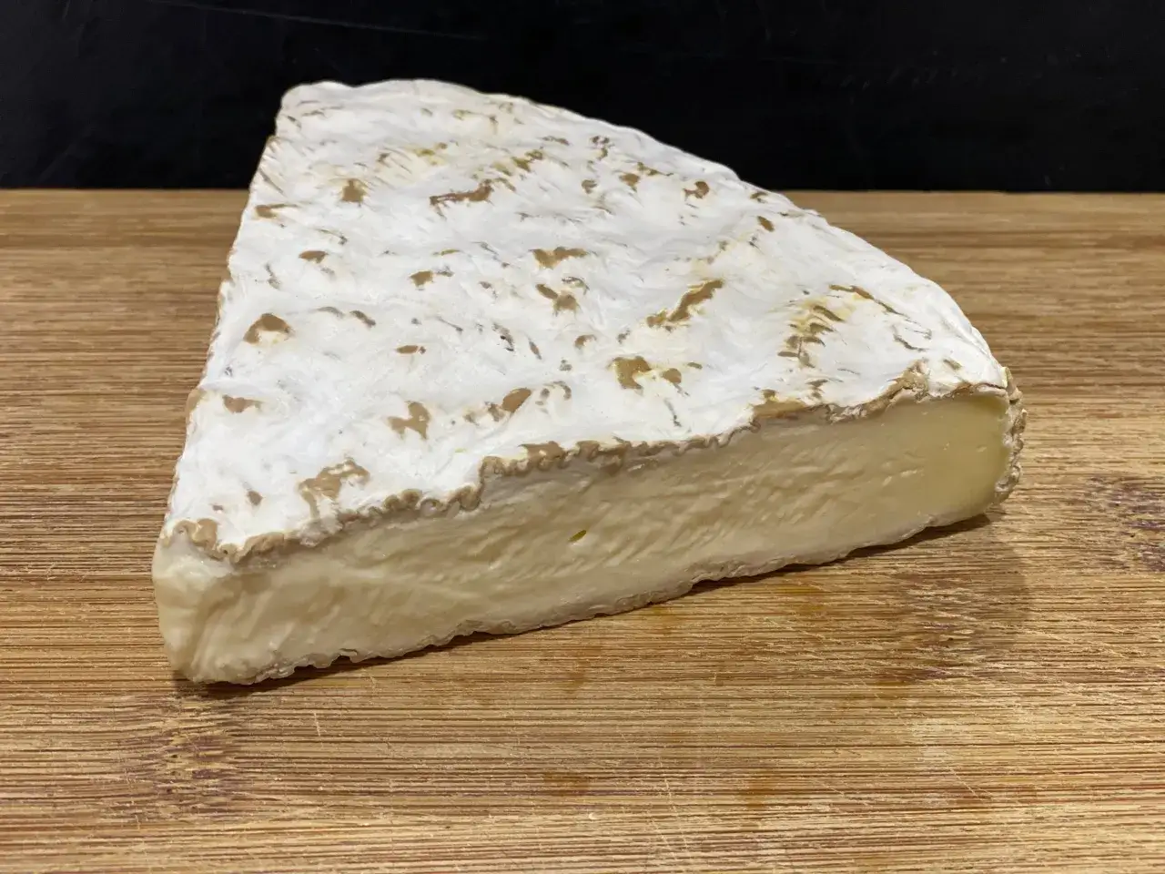 Un morceau de du brie cr&eacute;meux, &agrave; la cro&ucirc;te blanche et aux marbrures dor&eacute;es, repose sur une planche en bois.