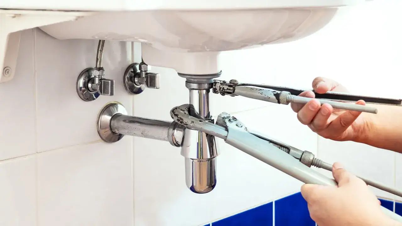 Mains tenant des cl&eacute;s pour d&eacute;monter le siphon de la baignoire.