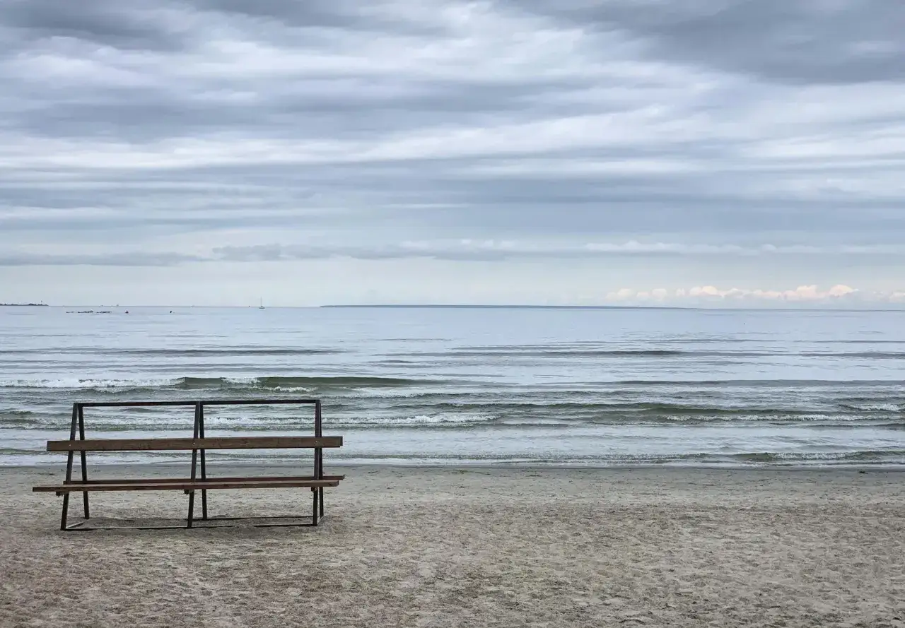 Pusta ławka na plaży, idealne ciche spokojne miejsce na weekend. Morze i zachmurzone niebo tworzą nastrój.