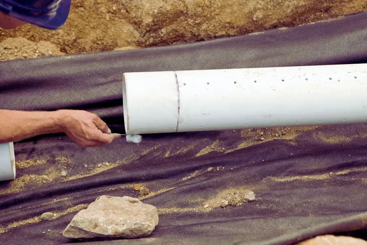 Main tenant enlever calcaire canalisation pvc, un ouvrier nettoie un tuyau blanc avec une petite brosse.