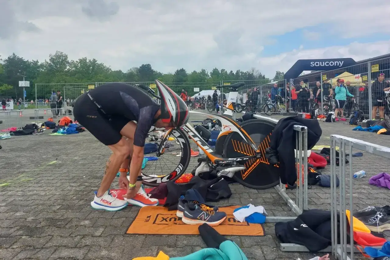 Triathlet bindet sich die Schuhe f&uuml;r den triathlon kurzdistanz. Rennrad und Ausr&uuml;stung liegen bereit.