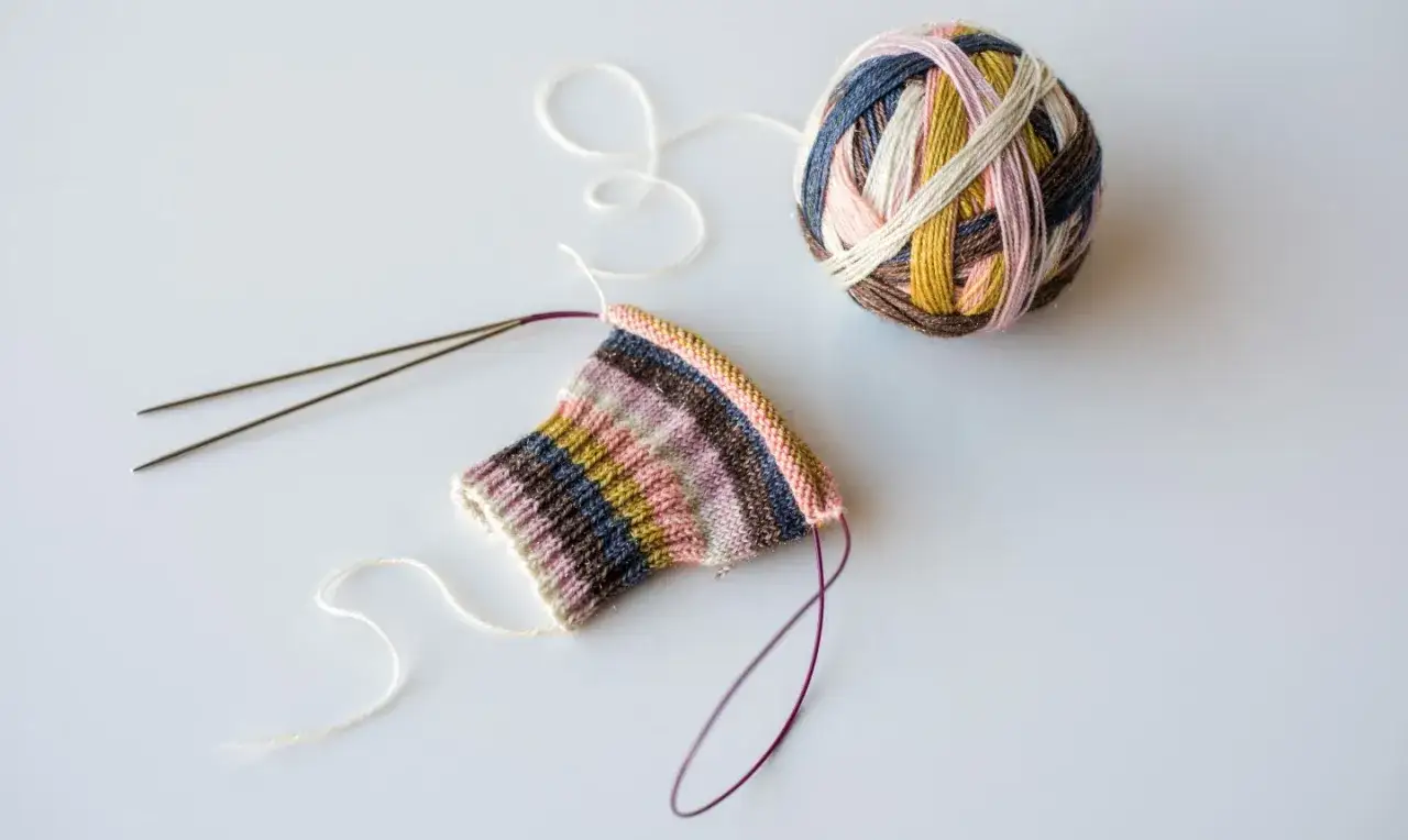 Tejiendo calcetines con agujas circulares. Ovillo de lana multicolor y pieza de tejido a rayas.