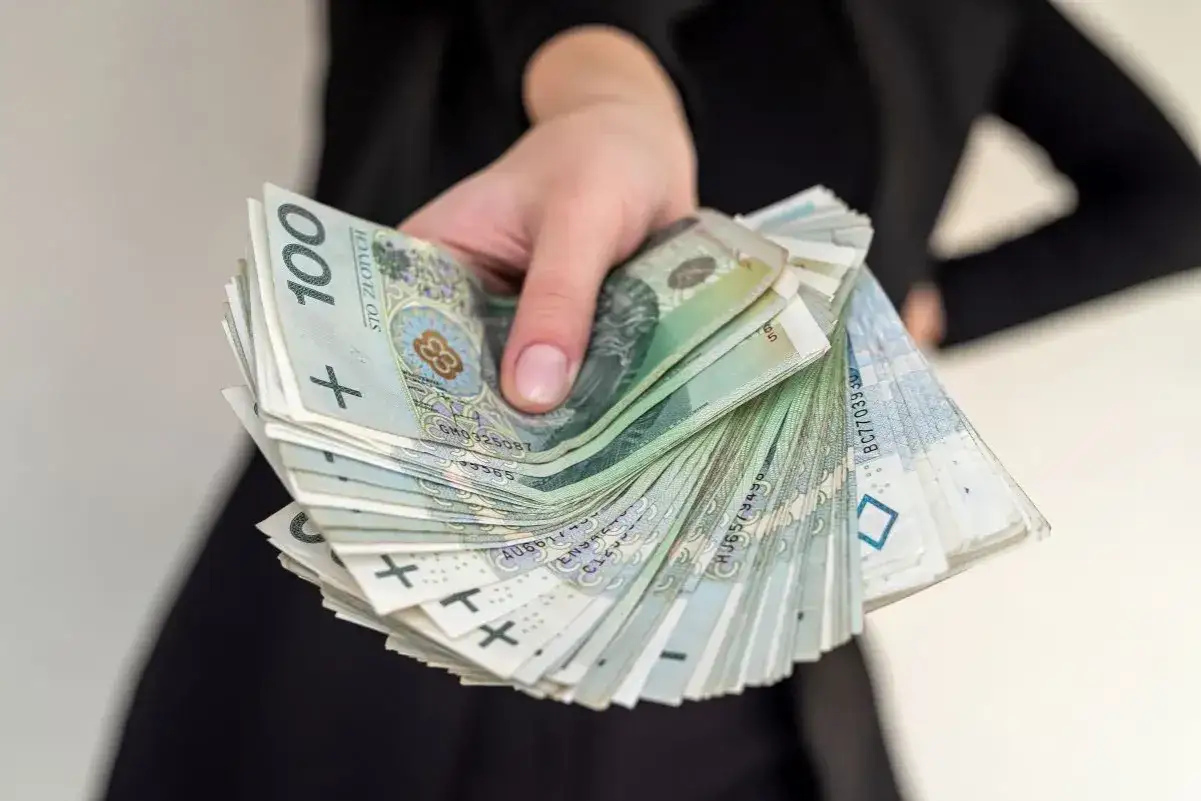 Dłoń trzyma plik banknotów 100 zł. Czy rencista może być opiekunem osoby niepełnosprawnej? Pieniądze to często klucz do godnego życia.