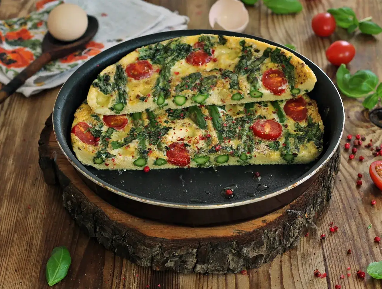Pyszny omlet ze szparagami i pomidorkami, posypany różowym pieprzem, podany na drewnianej desce.