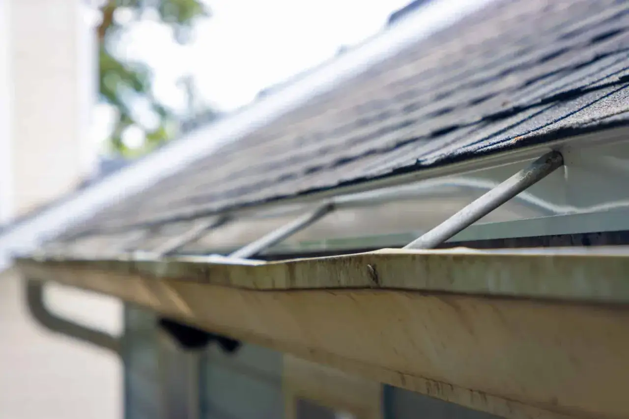 A close-up of a dirty gutter, showing the need for a gutter fix. Metal supports are visible, holding the gutter in place.