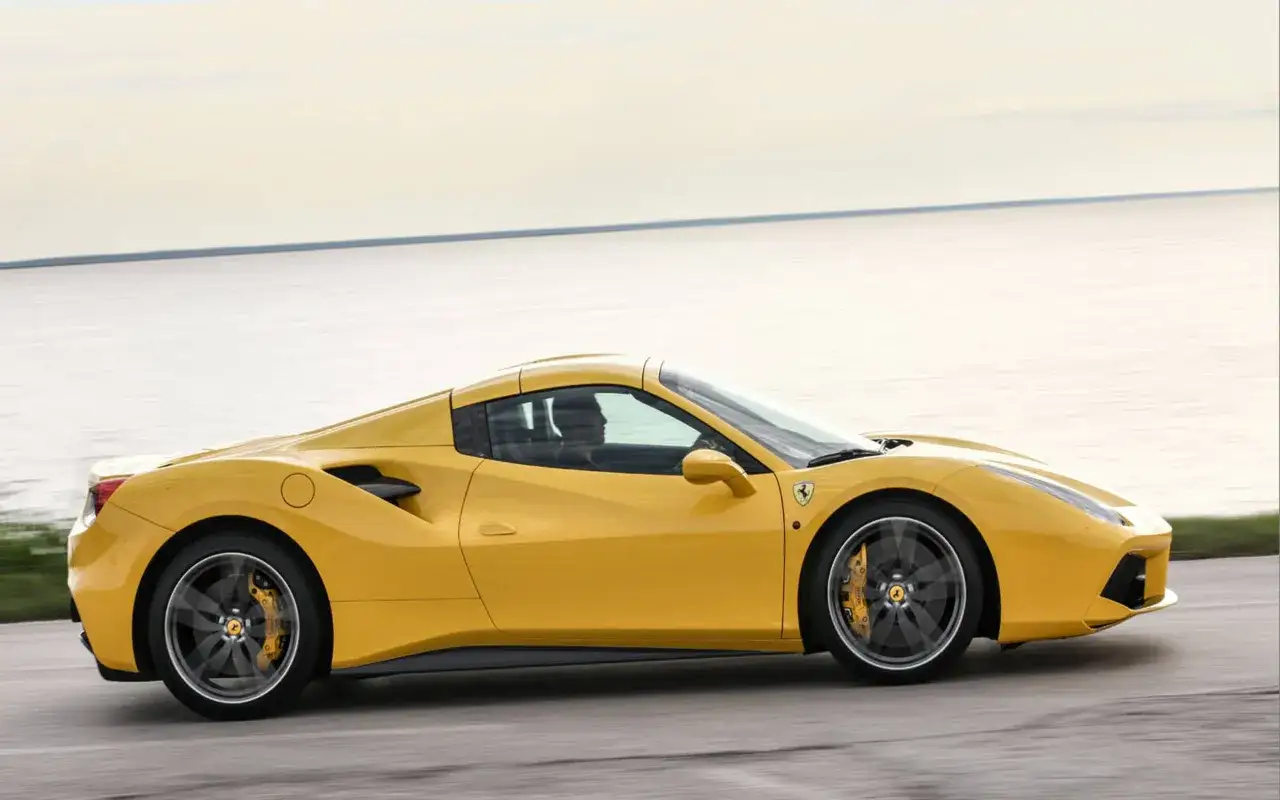 Żółte Ferrari 488 pędzi wzdłuż wybrzeża, jego sylwetka lśni w słońcu.