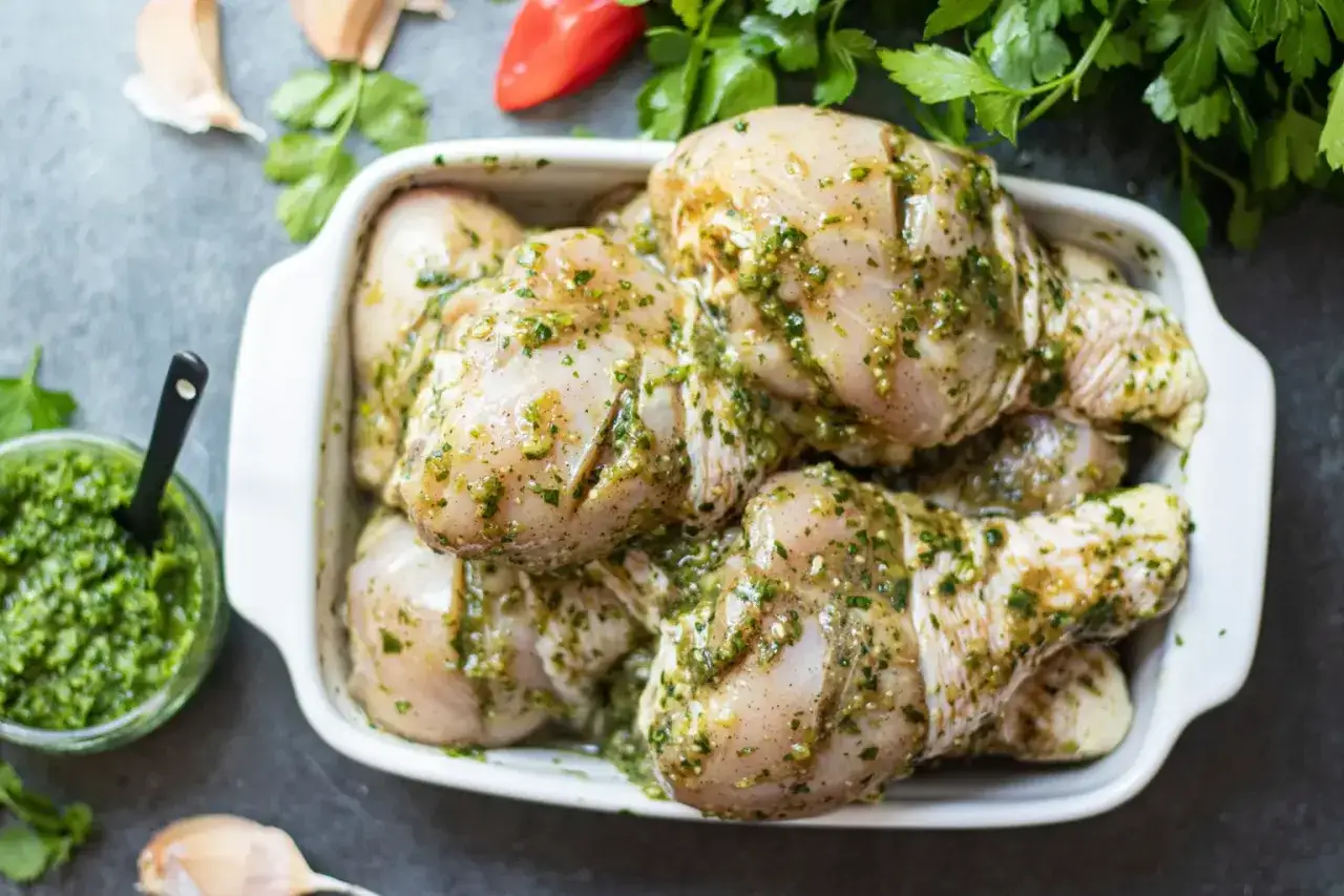 Cuisses de poulet crues dans un plat blanc, recouvertes d'une marinade verte aux herbes. Pr&ecirc;tes pour la cuisson.
