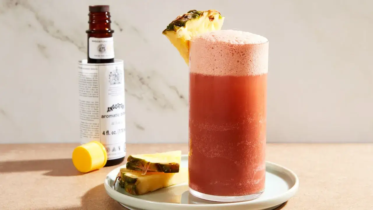 Szklanka orzeźwiającego drinka z ananasem i pianką, obok buteleczka Angostura Aromatic Bitters.