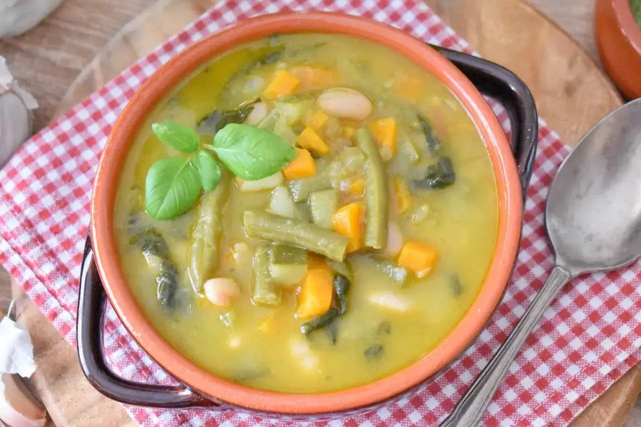 Aromatyczna zupa minestrone Magdy Gessler, pełna warzyw i fasoli, ozdobiona listkiem bazylii.