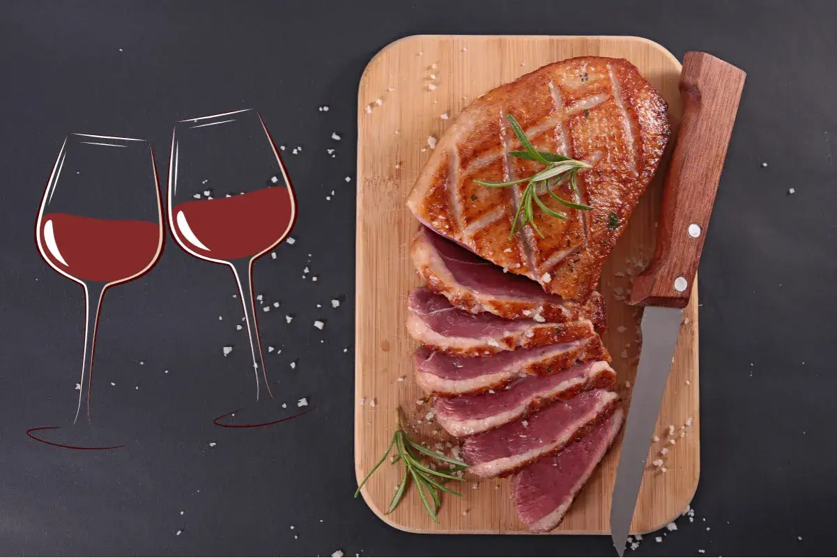 Magret de canard tranch&eacute; sur planche en bois, accompagn&eacute; de deux verres de vin rouge. La question 
