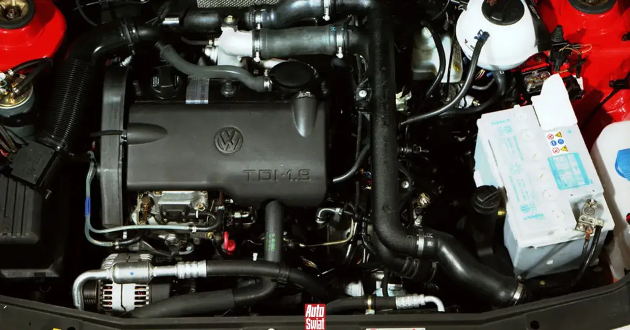Silnik TDI 1.9 Volkswagena, z widocznym logo i oznaczeniem na pokrywie. Widać turbosprężarkę, akumulator i inne elementy układu napędowego.