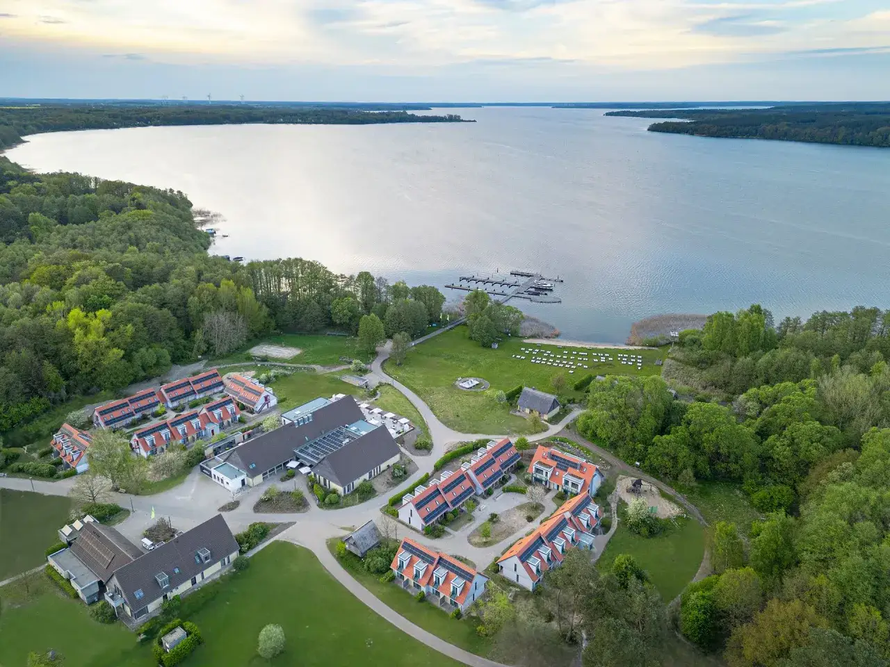 Ferienanlage am Plauer See mit roten Dächern, Bootssteg und viel Grün. Das Beech Resort Plauer See lädt zum Entspannen ein.