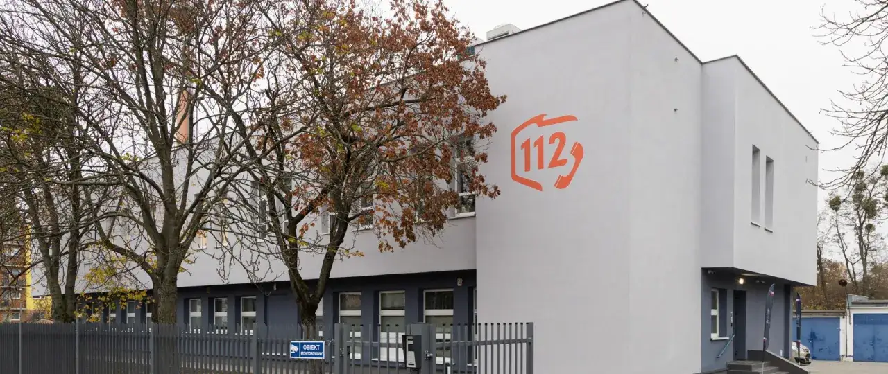 Budynek z pomarańczowym logo 112. To miejsce, gdzie pracuje dyspozytor, kt&oacute;ry odbiera zgłoszenia i wysyła pomoc.