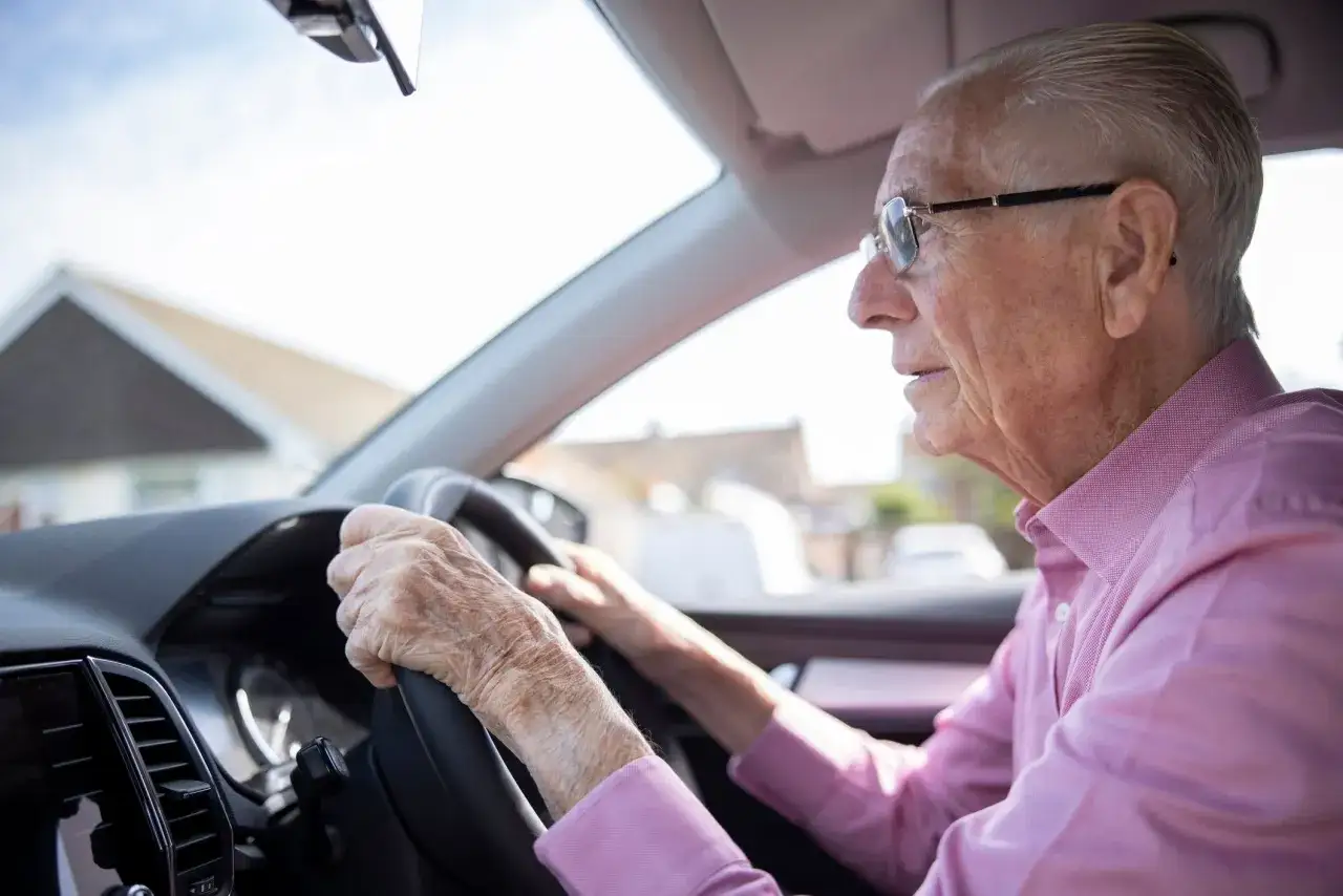 Un homme âgé au permis de conduire senior, lunettes sur le nez, conduit prudemment sa voiture.