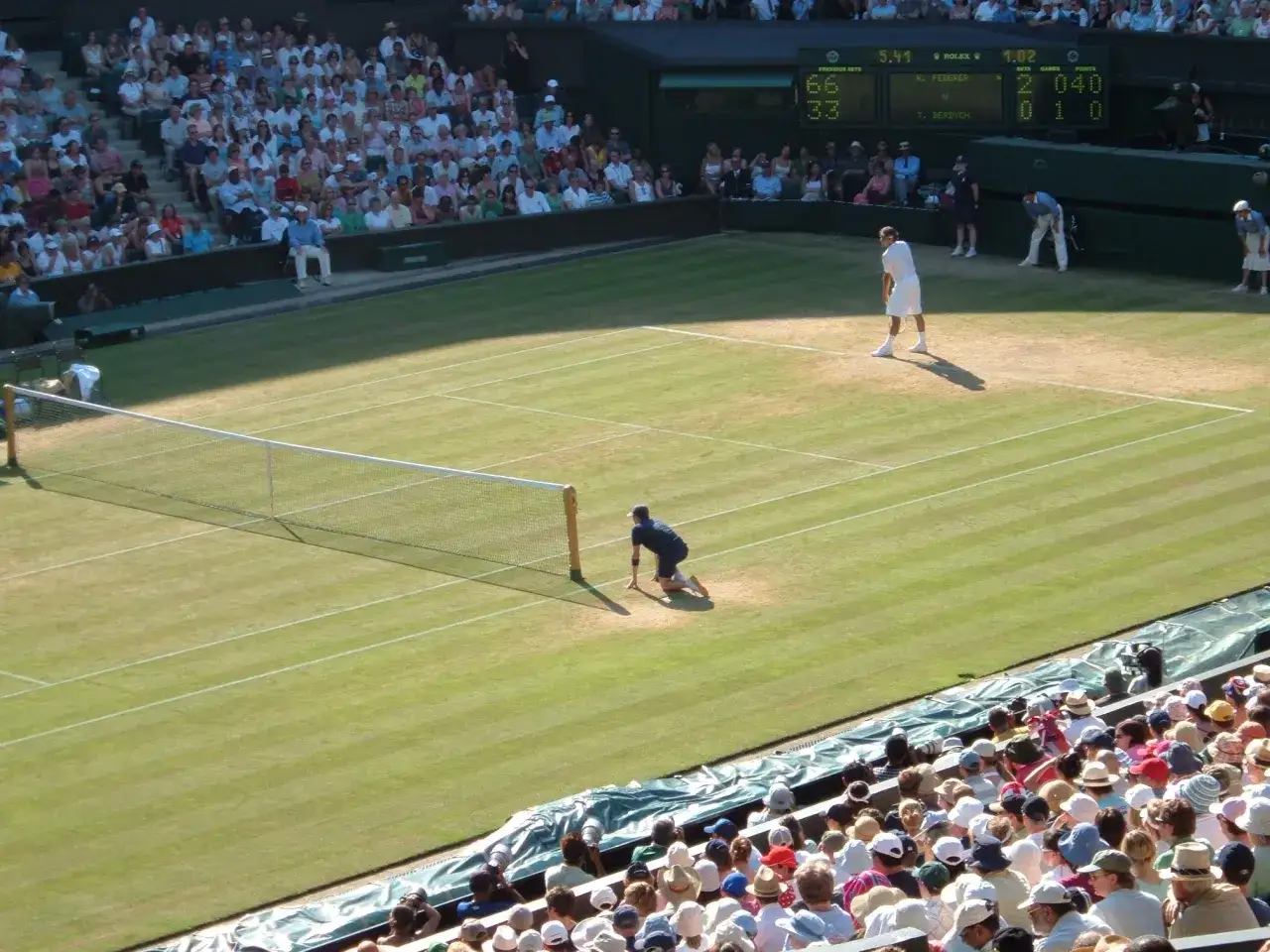 Gracze na trawiastym korcie podczas meczu tenisowego Wimbledon. Widownia obserwuje z trybun.