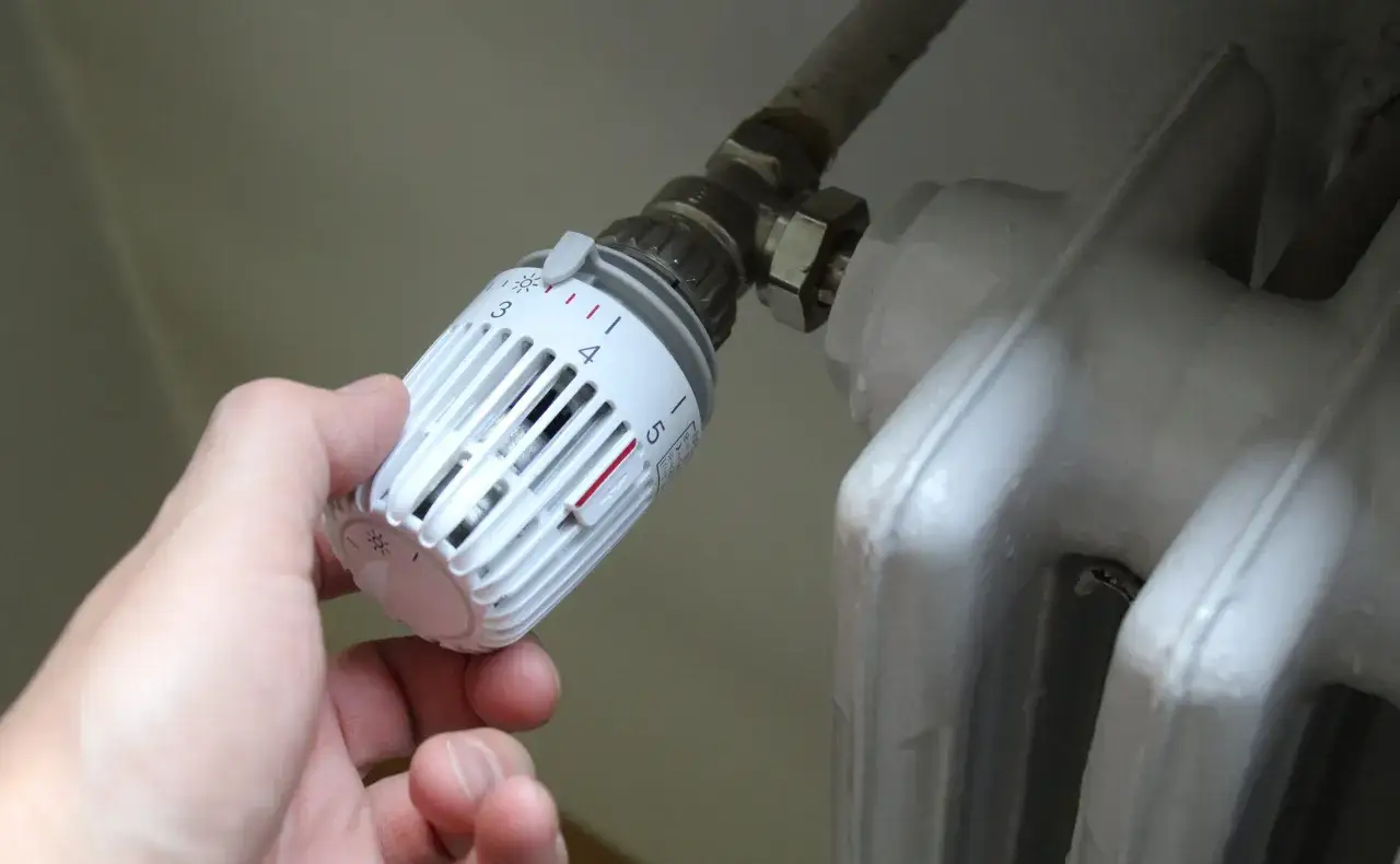 Mano che regola la temperatura del riscaldamento a radiatori. La manopola bianca è impostata su 3.
