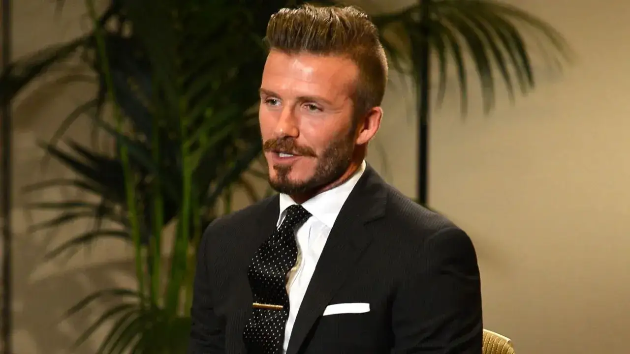 David Beckham w garniturze, z krawatem i spinką do krawata. Pokazuje, jak nosić spinkę do krawata, by wyglądać elegancko.
