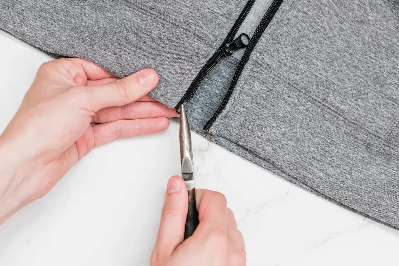 Manos arreglan pistón cremallera de sudadera gris con alicates.