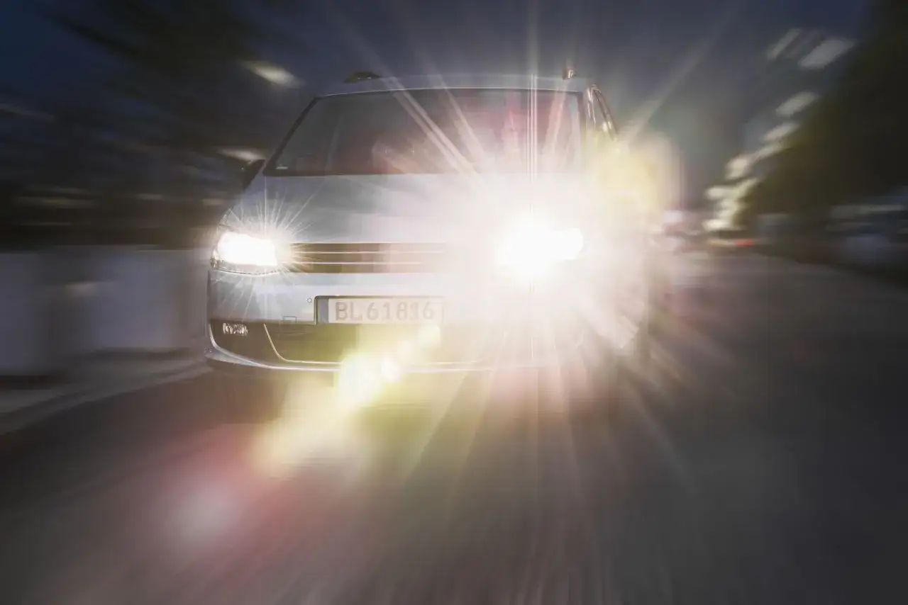 Un occhio solo, abbagliato dai fari di un'auto che sfreccia nella notte. La luce intensa crea un alone quasi mistico.