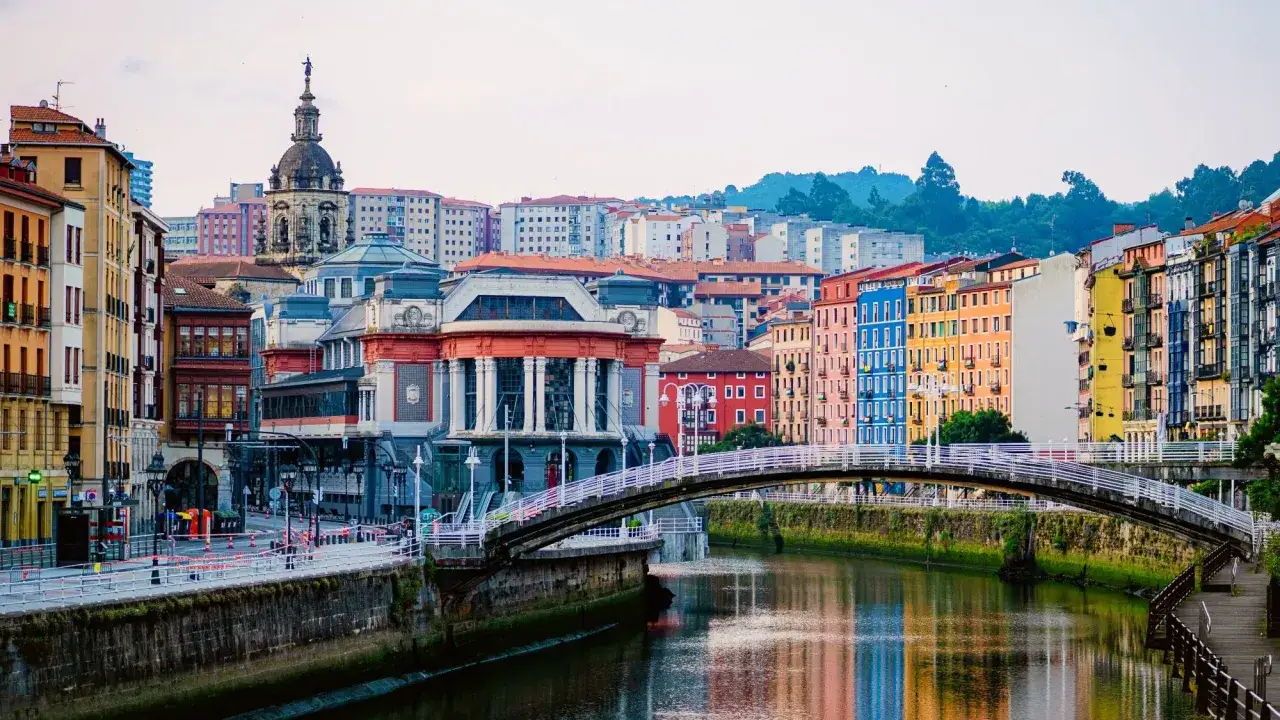 Un puente blanco cruza un río reflejando coloridas fachadas. Ideal para saber qué ver en Bilbao en 2 días.