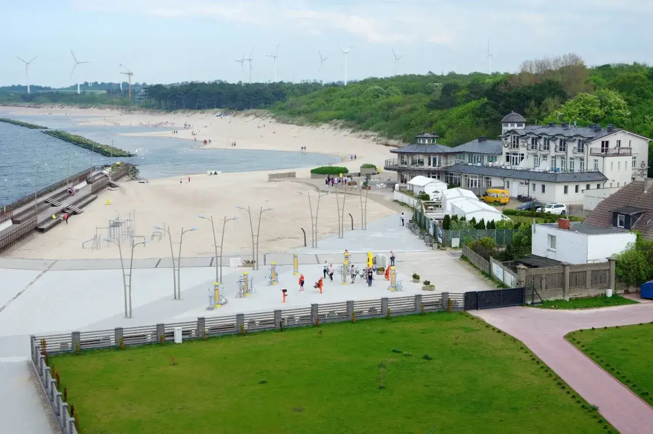 Widok na miasto przy ujściu Wieprzy do Bałtyku. Plaża, deptak z siłownią plenerową i budynki hotelowe.