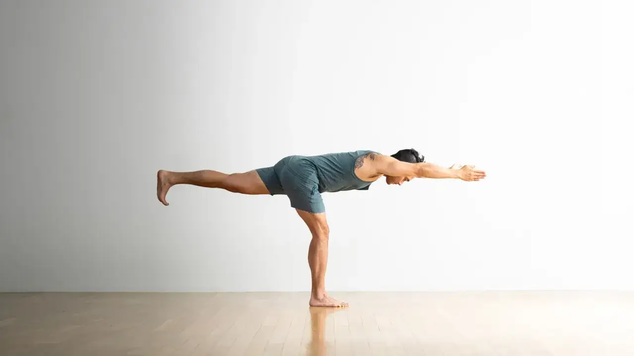 Hombre en postura de yoga Virabhadrasana 3, equilibrado sobre una pierna, con el cuerpo extendido horizontalmente.