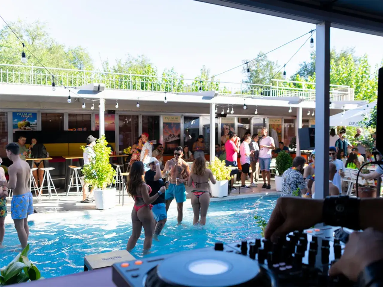 Gente disfrutando de un tardeo techno en Madrid, bailando y refrescándose en una piscina.
