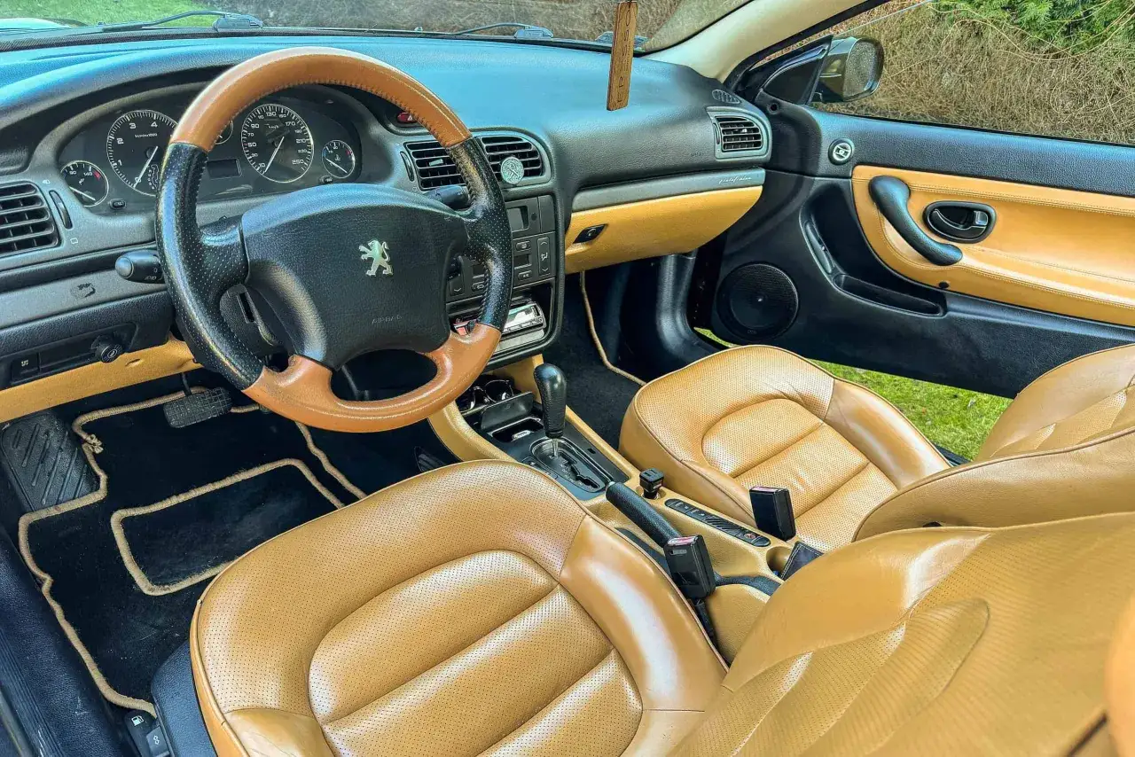 Wnętrze 406 coupe z beżową skórzaną tapicerką i czarnymi dywanikami. Kierownica dwukolorowa, deska rozdzielcza z licznymi wskaźnikami.