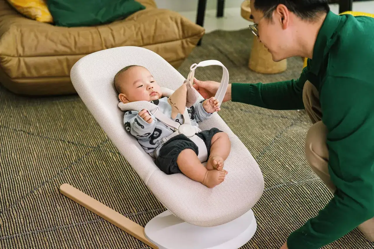 En pappa interagerar med sitt barn i en Stokke babysitter. Babysittern är bekväm och ger barnet en trygg plats att vila och leka.