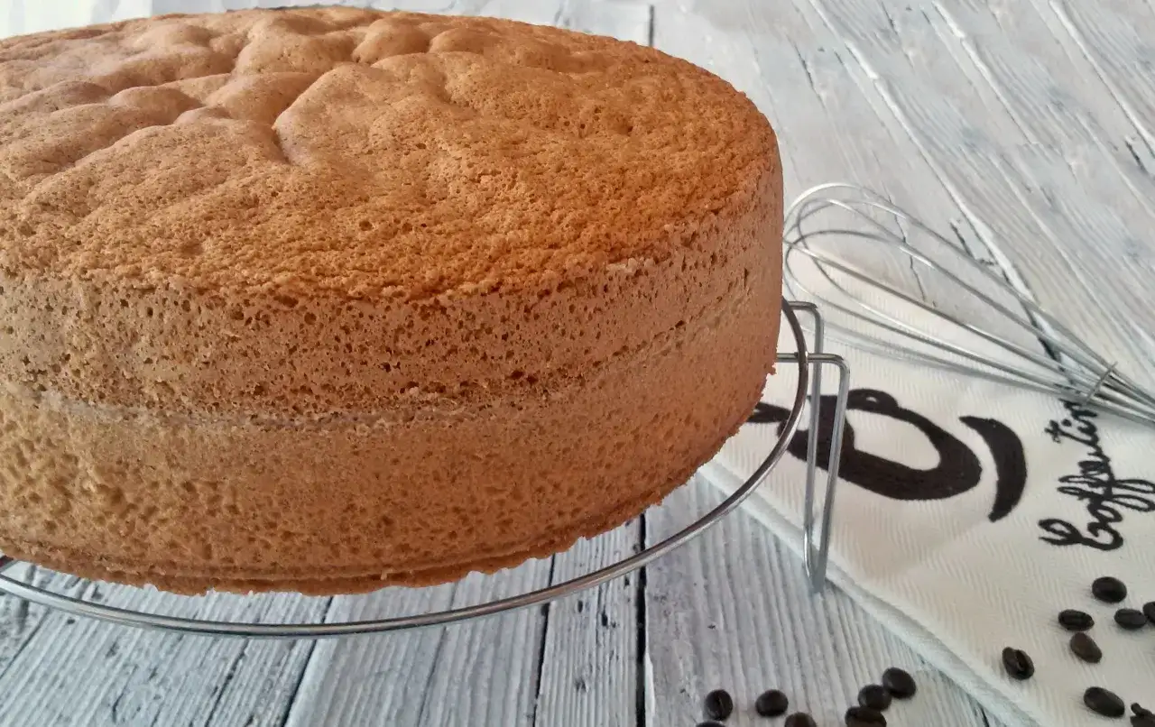 Una soffice base per torta, pronta per essere trasformata in una deliziosa bagna al caff&egrave;. Accanto, un frustino e chicchi di caff&egrave;.
